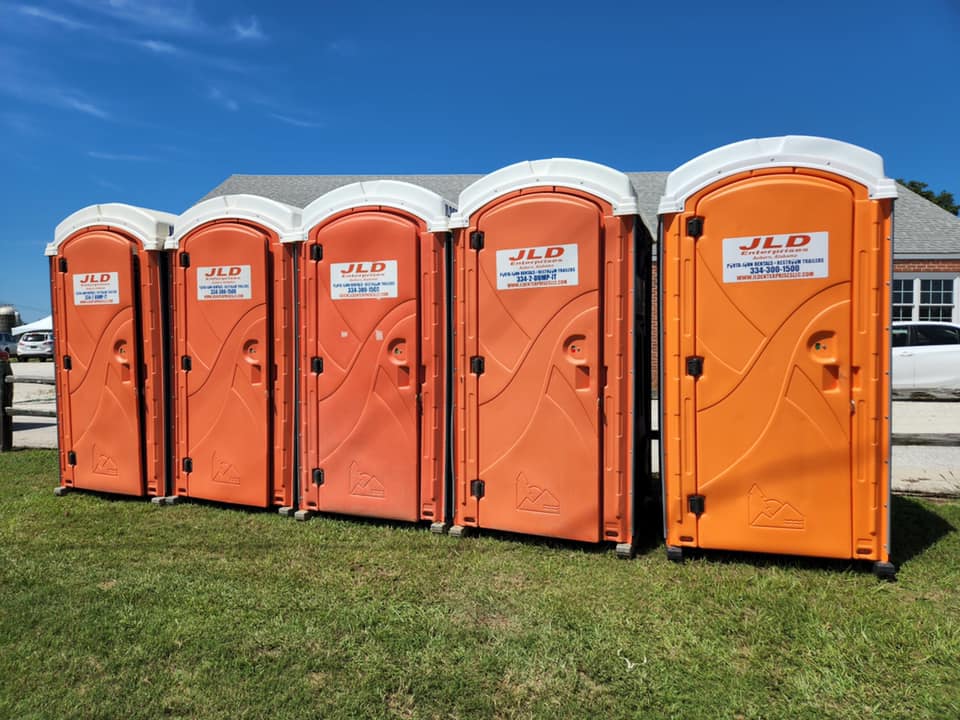 Orange portable restrooms on a grassy lot in Auburn, AL under a clear blue sky.