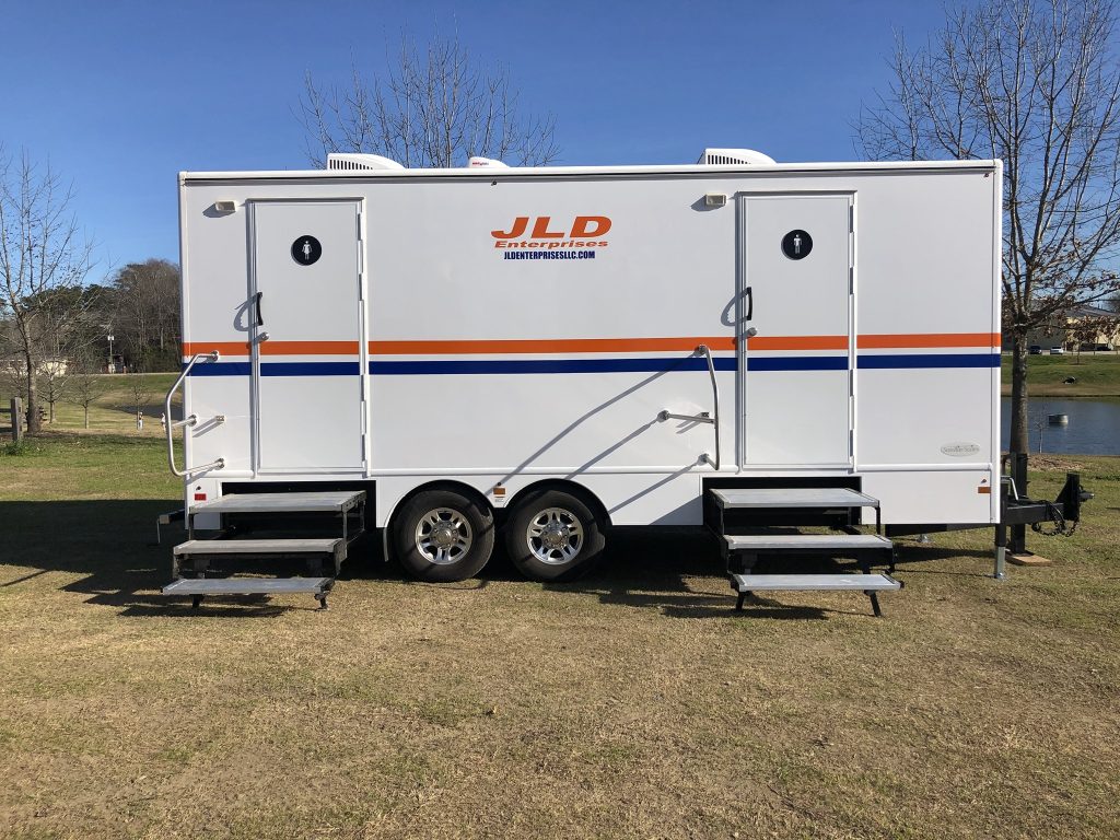 Portable restroom trailer in Auburn, AL park setting, blue sky background.
