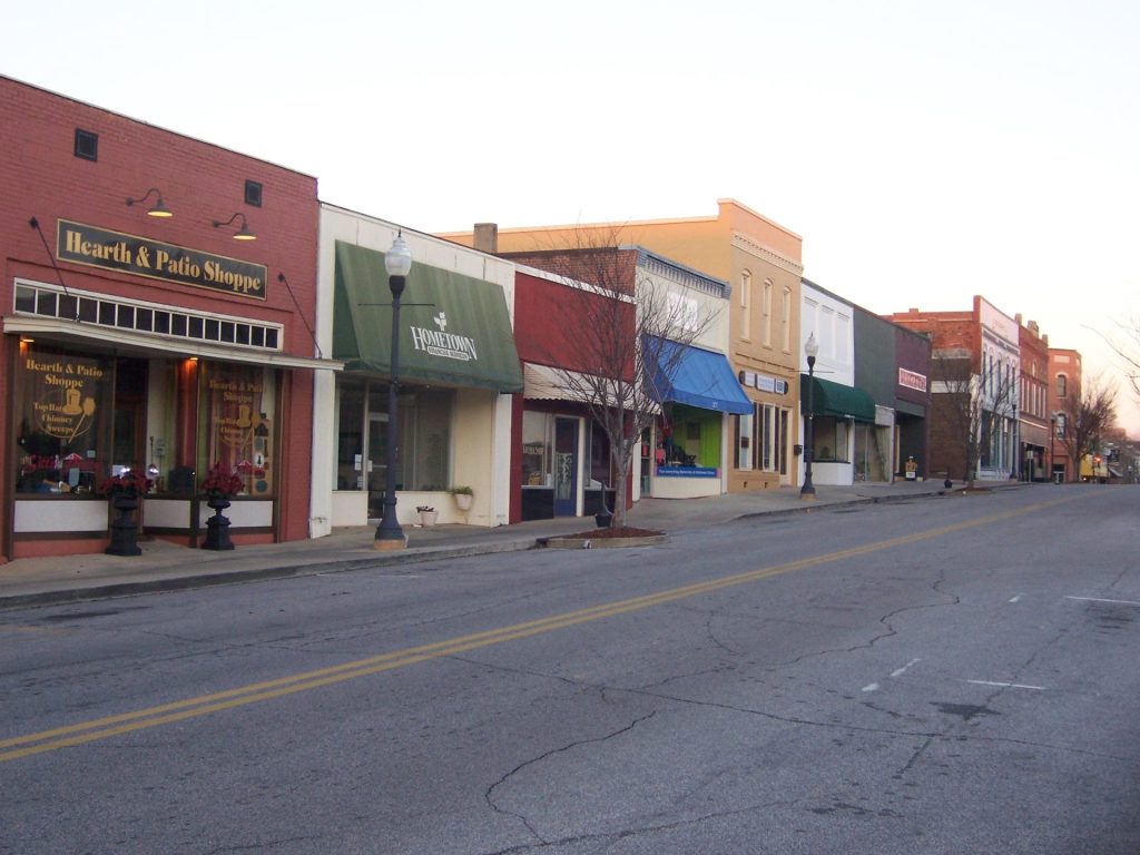 Scenic view of a quaint downtown street in Auburn, AL, lined with colorful storefronts under a clear sky.