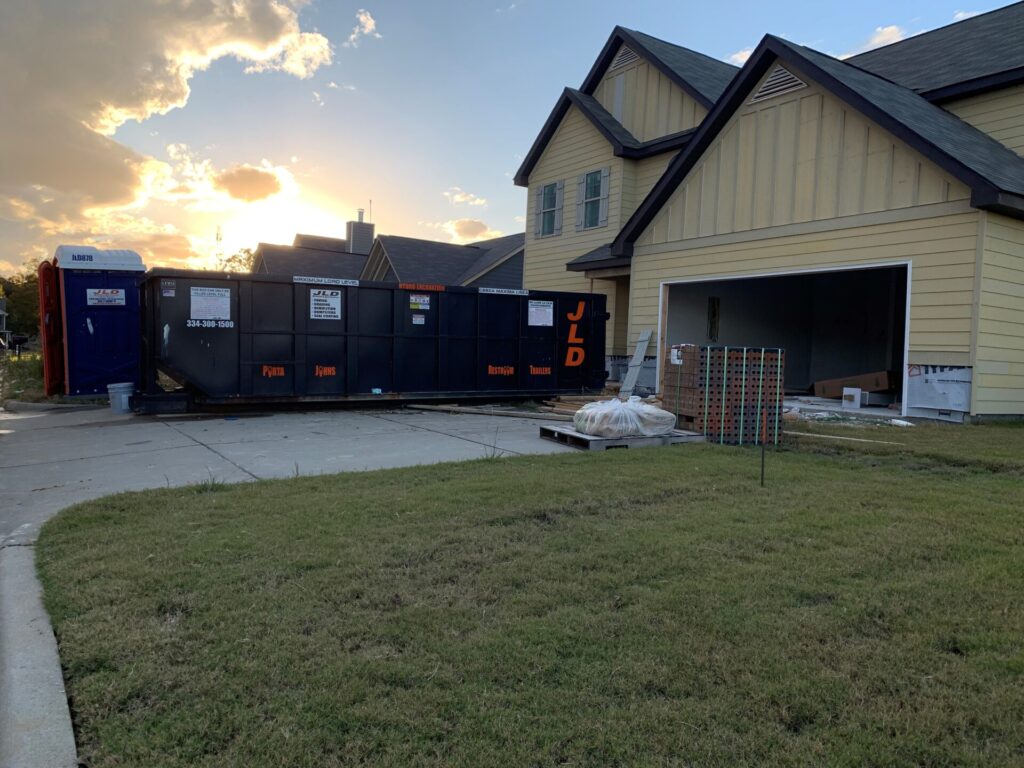 Construction site with a yellow house and dumpster in Auburn, AL, at sunset.